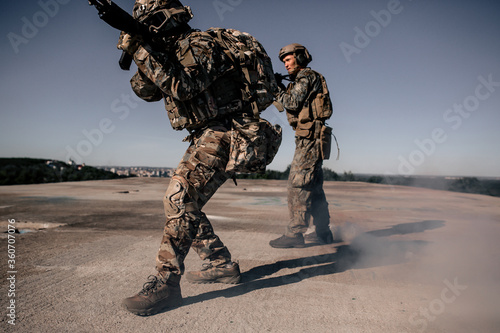 Two us army soldiers in camouflage standing on the roof of a building with a rifle aiming at opponents in the fog