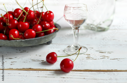 Strong alcoholic cherry drink Kirsch or Kirschwasser -  in a glass and fresh cherry on the white wooden table
