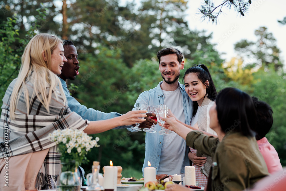 Fototapeta premium Young joyful friends of various ethnicities cheering up with glasses of wine