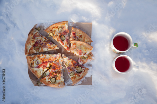 Winter picnic: slices of pizza and two cups of tea on the snow