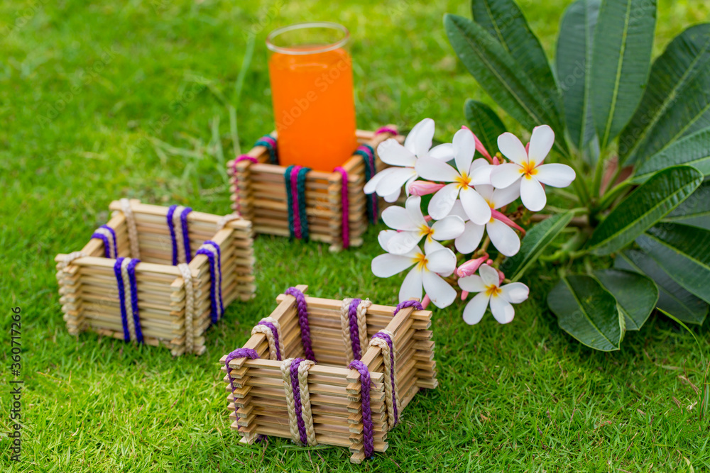 Bamboo sticks glass holder with a glass of orange juice on grass background. Bamboo sticks glass holder with a glass of orange juice on grass background.