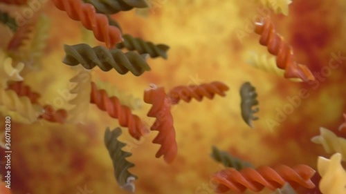 Dry colored pasta fusili flying diagonally on a yellow ochre background in slow motion photo