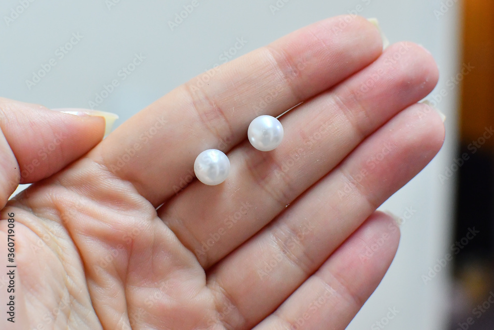 Female hand holding white colored freshwater pearl earring studs Female hand holding white colored freshwater pearl earring studs