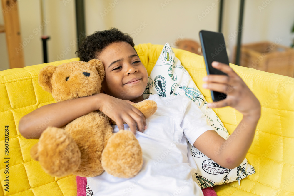 Cute little boy of African ethnicity embracing his teddybear while making selfie Cute little boy of African ethnicity embracing his teddybear while making selfie