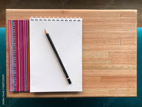 Pencil with a sketchbook on a woden table and a small plant photo