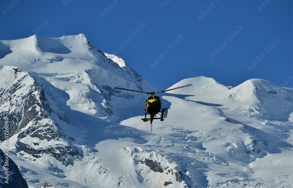 Close up of a helicopter in action against a blue sky with snowy mountains in the background