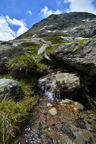 Mountain river flows over stones in the meadow with blue sky and white clouds