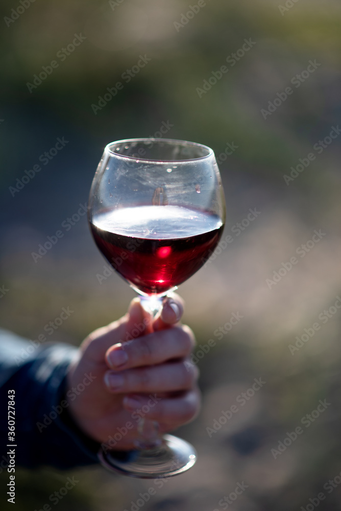 on a blurred background of green grass a glass with red wine in hand