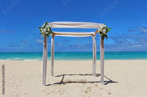 Tropical wedding arrangement in Hawaii, Waimanalo beach - White wedding arch with beautiful flowers on the white sandy beach with turquoise sea in the background. photo