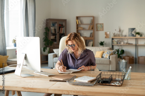 Busy mature female in eyeglasses and casualwear writing down working plan points