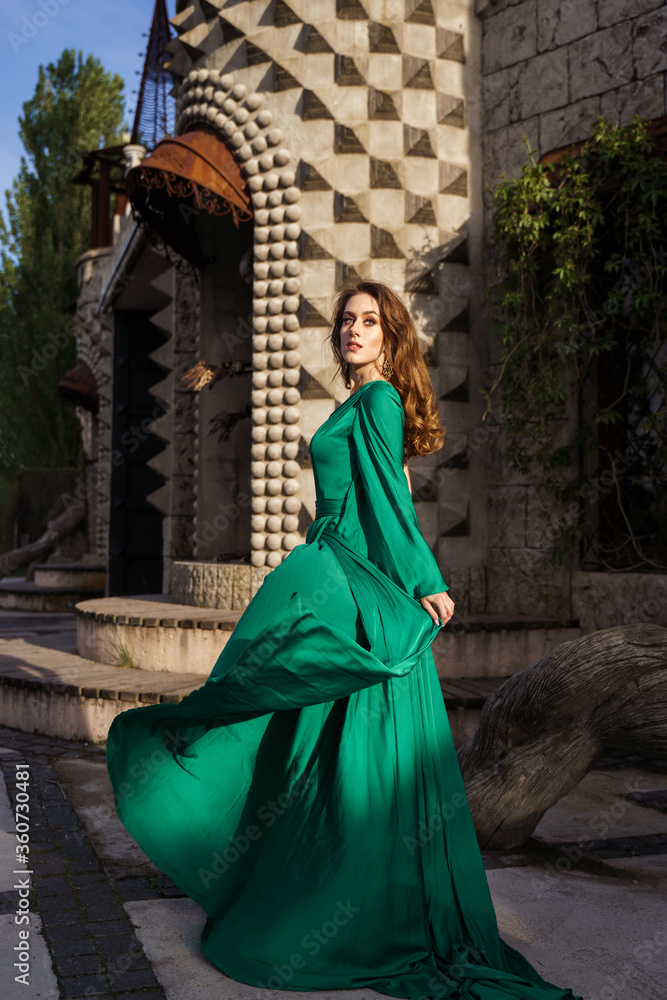 Naklejka premium beautiful young woman in long green dress standing posing against the backdrop of a fairytale castle