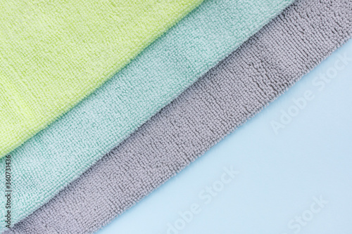 Gray, blue and yellow microfiber cloth for cleaning on blue background. Cleaning micro fabric towels for dusting and polishing. Domestic household cleaning service concept. Close up, copy space