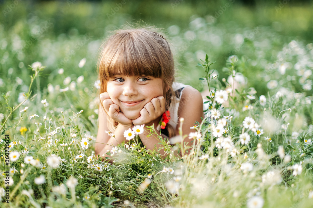 Pretty girl lying in daisy field and smiling to camera, unity with nature, childhood Pretty girl lying in daisy field and smiling to camera, unity with nature, childhood