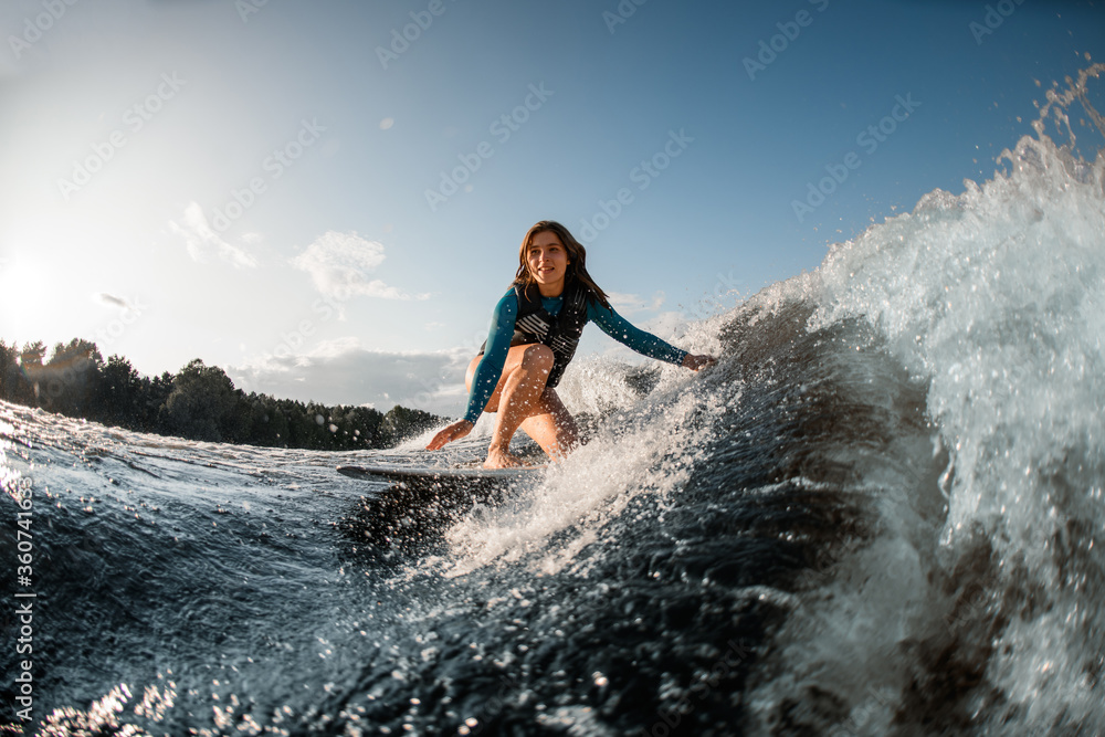 smiling young woman wakesurfing down the river waves