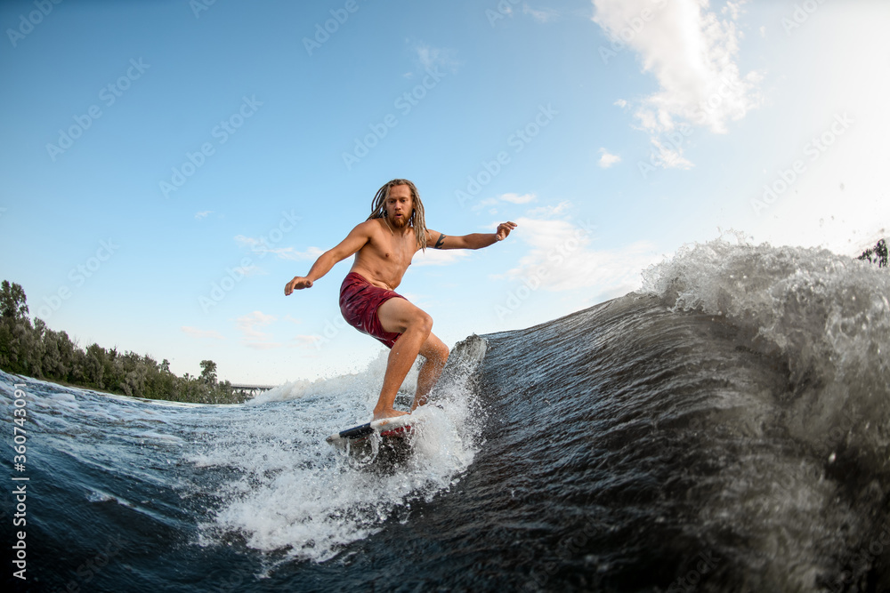 young man wakesurfer with dreadlocks ride the waves on surfboard.