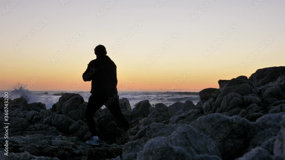 Men warrior monk practicing silhouette tai chi karate kung Fu on the rocky stones horizon at sunset or sunrise. Art of self-defense. Silhouette on a background of dramatic epic waves at pacific coast Men warrior monk practicing silhouette tai chi karate kung Fu on the rocky stones horizon at sunset or sunrise. Art of self-defense. Silhouette on a background of dramatic epic waves at pacific coast
