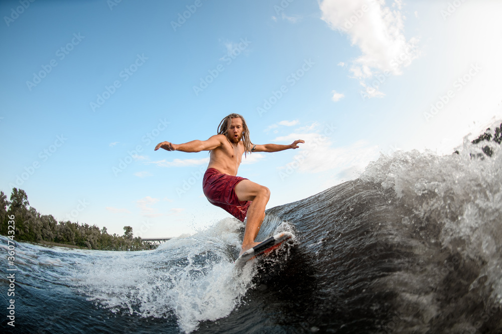 young active man with dreadlocks ride the waves on surfboard.