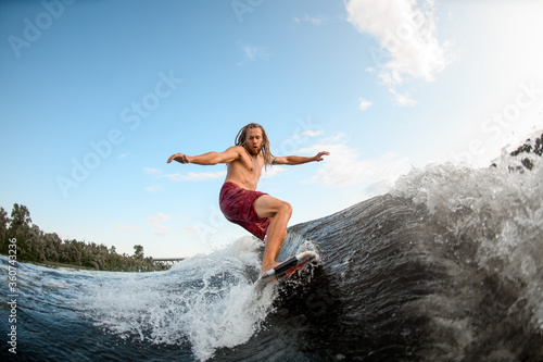 young active man with dreadlocks ride the waves on surfboard.