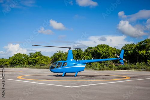 Blue helicopter landing on asphalt helipad 