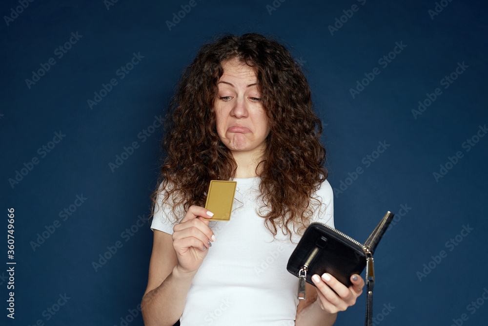 Internet banking, commerce concept. Upset young curly haired female with poring lips, can not use credit card for online shopping, has not enough money on her account. Disappointed female indoors.