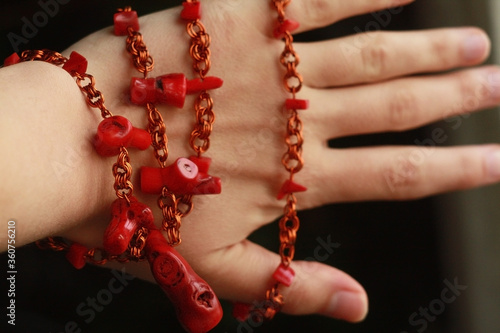 Red beads made of natural coral and copper wire on a female hand .