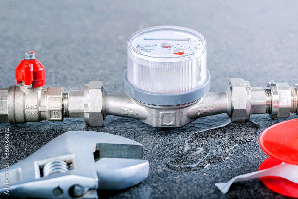Water meter with leak of water and wrench on grey background. Concept broken pipeline, meter. Water meter with leak of water and wrench on grey background. Concept broken pipeline, meter.