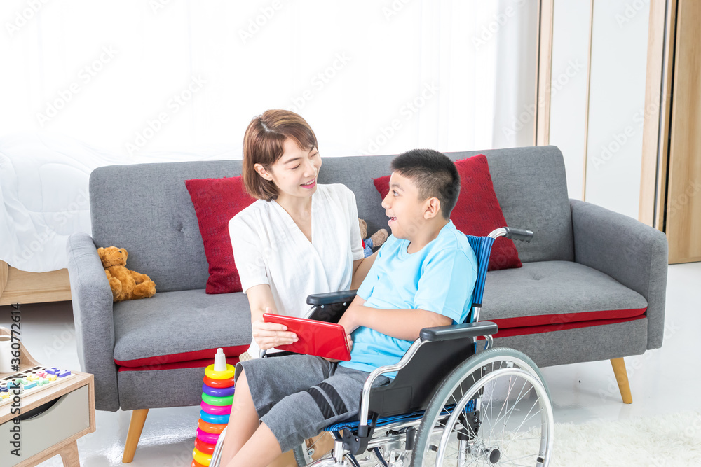 asian woman playing with disabled child on wheelchair via tablet in living room. asian woman playing with disabled child on wheelchair via tablet in living room.