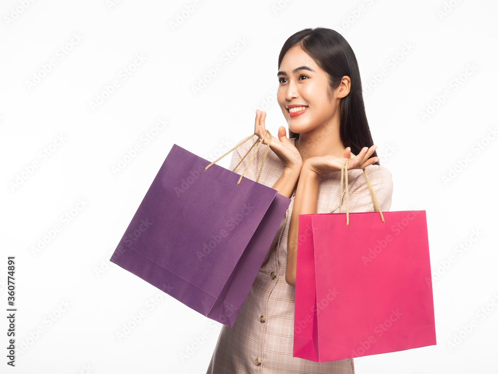 Portrait of an excited beautiful asian woman wearing dress and holding shopping bags isolated on white background.