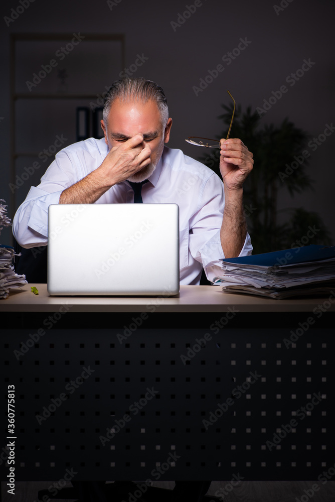 Old male employee working late at workplace Old male employee working late at workplace
