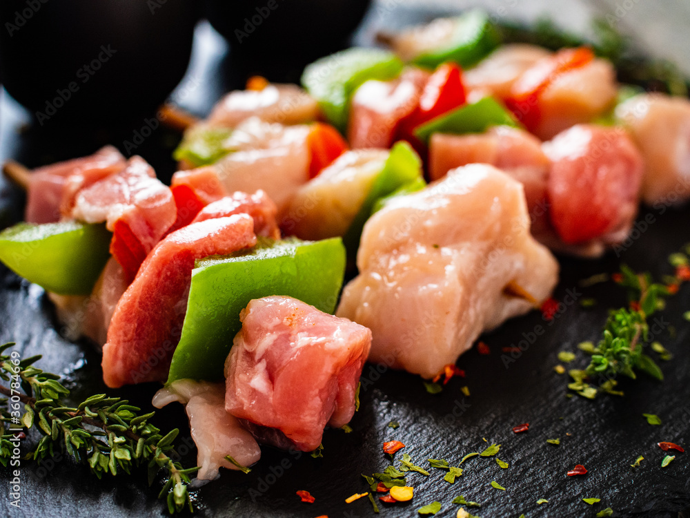 Uncooked shashlik and seasonings on black stone board on wooden table Uncooked shashlik and seasonings on black stone board on wooden table