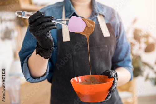 Pastry chef young woman in apron prepares sweet candies, melts chocolate in bowl