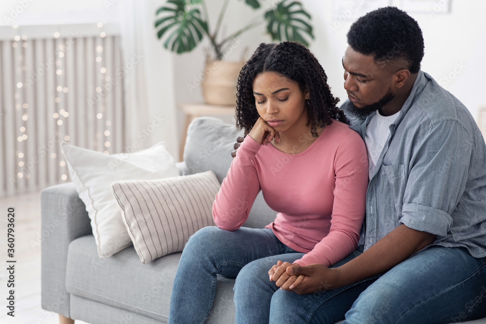 Caring Afro Man Comforting His Depressed Wife At Home, Embracing And Supporting Caring Afro Man Comforting His Depressed Wife At Home, Embracing And Supporting
