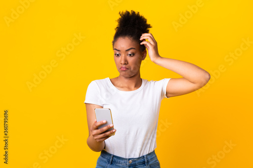 Confused young african woman using mobile phone