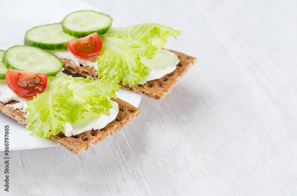 Fresh summer healthy appetizer of whole grain rye crisps breads with vegetables - green salad, cucumber, tomato, cream cheese on white wood board, closeup, copy space. Fresh summer healthy appetizer of whole grain rye crisps breads with vegetables - green salad, cucumber, tomato, cream cheese on white wood board, closeup, copy space.