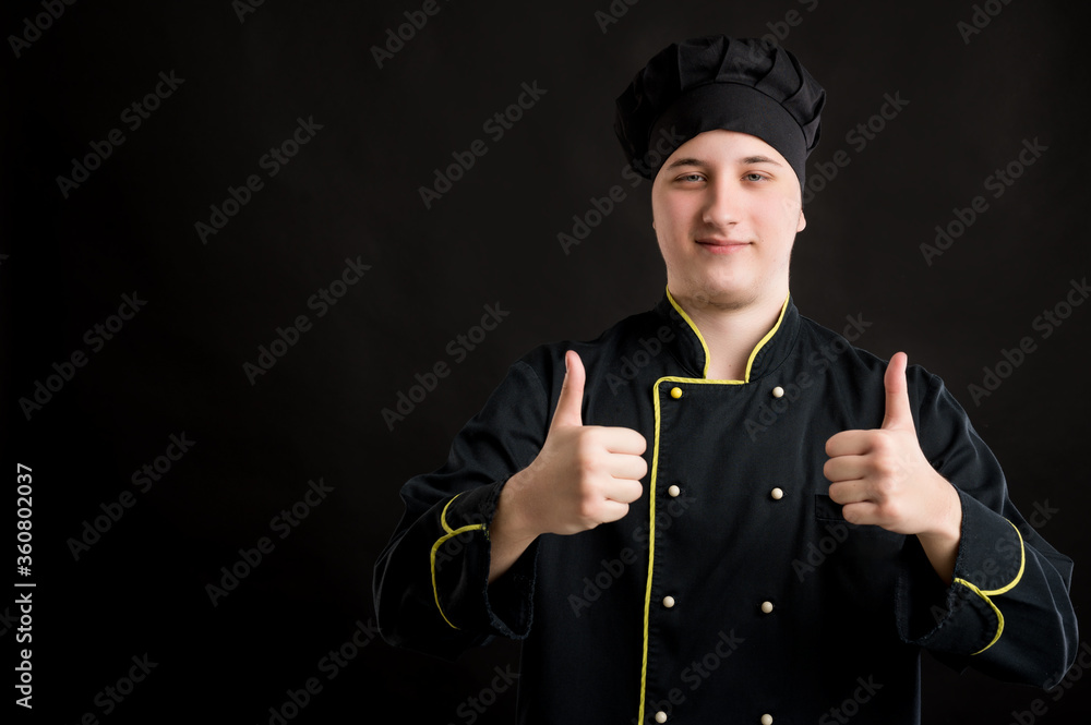 Young male dressed in a black chef suit showing thumbs up with both hands Young male dressed in a black chef suit showing thumbs up with both hands