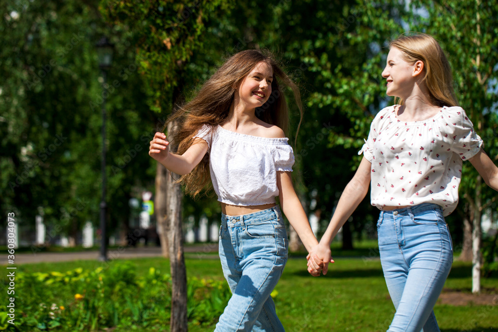 Two happy girlfriends teenagers are walking in the summer park.