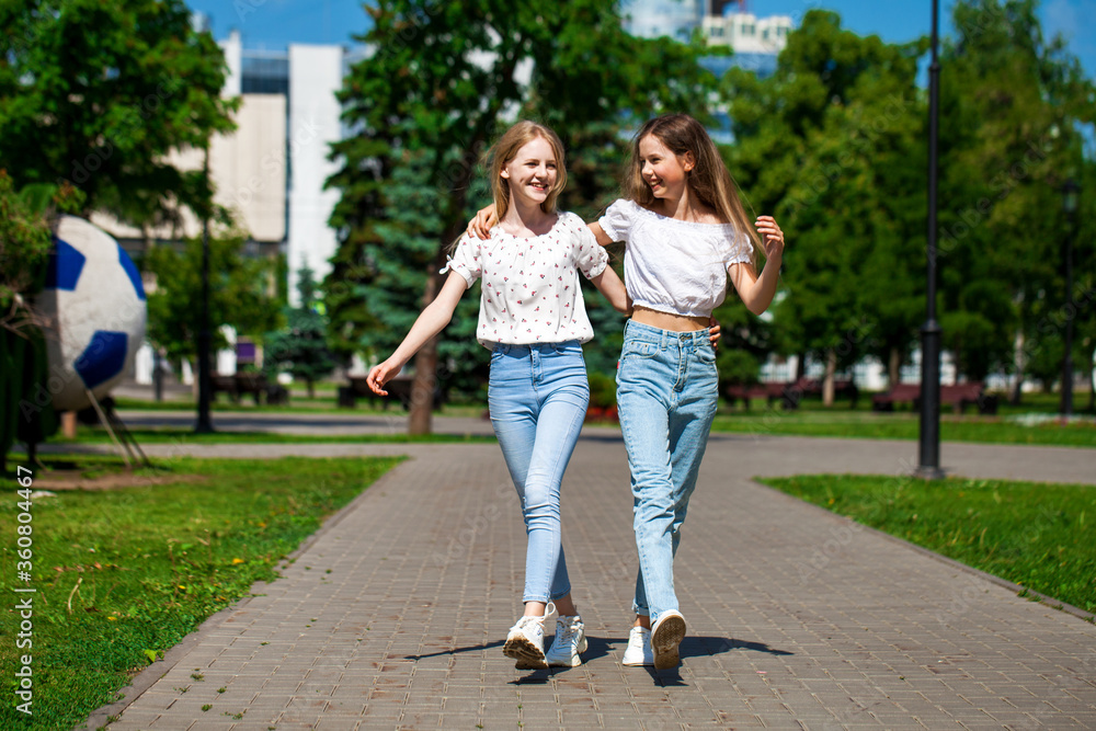 Two happy girlfriends teenagers are walking in the summer park. Two happy girlfriends teenagers are walking in the summer park.