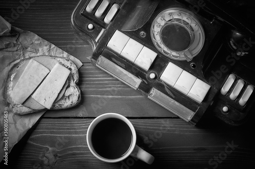 Breakfast on the desktop many years ago. Old telephone sandwich on crumpled paper coffee in a cup on a wooden table in black color.