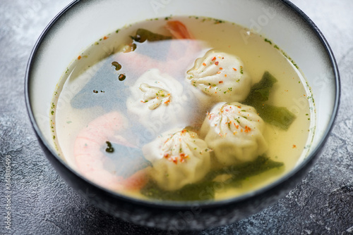 Bowl of wontons with shrimps in a broth over grey stone background, selective focus, studio shot