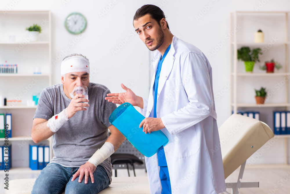 Fototapeta premium Young male doctor and old patient in first aid concept