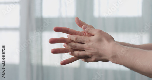 man apply liquid sanitizer on his hands standing in front of the window closeup