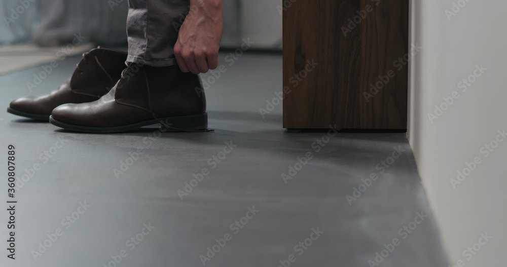 Fototapeta młody człowiek zdejmuje swoje brązowe skórzane buty chukka w pomieszczeniu