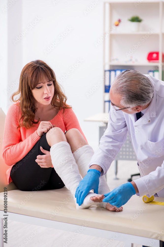 Fototapeta premium Young leg injured woman visiting old doctor traumatologist