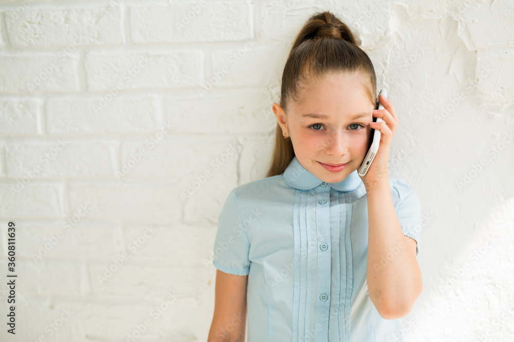beautiful young teenage girl on a background of a white wall with a phone in her hand beautiful young teenage girl on a background of a white wall with a phone in her hand