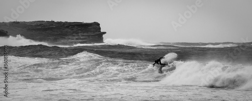 Grayscale shot of a surfer surfing in the waves of a sea
