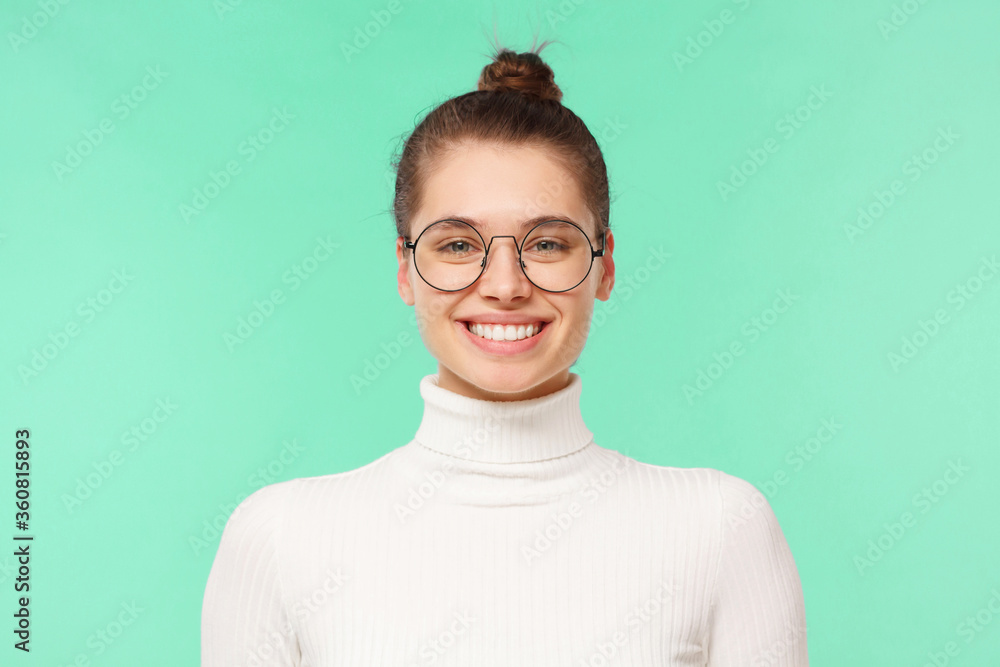 Young student girl in eyeglasses and white sweater, feeling confident and smiling happily, happy with working day, isolated on mint blue background Young student girl in eyeglasses and white sweater, feeling confident and smiling happily, happy with working day, isolated on mint blue background
