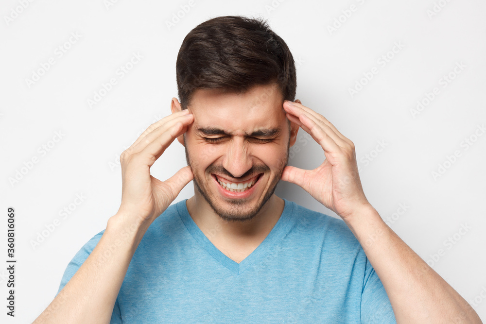 Close up portrait of man touching temples with closed eyes, trying to relieve strong headache, feeling stressed and exhausted, isolated on gray background Close up portrait of man touching temples with closed eyes, trying to relieve strong headache, feeling stressed and exhausted, isolated on gray background