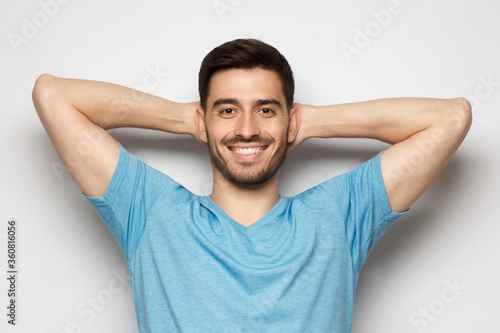 Young man standing isolated on gray background with arms behind head, relaxing peacefully in free time