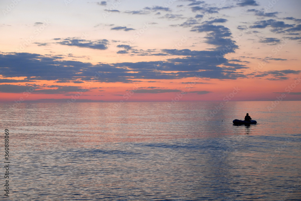 Sunrise seascape. Lonely fisherman on the boat in the middle of Caspian Sea. Derbent, Dagestan, North Caucasus, Russia.