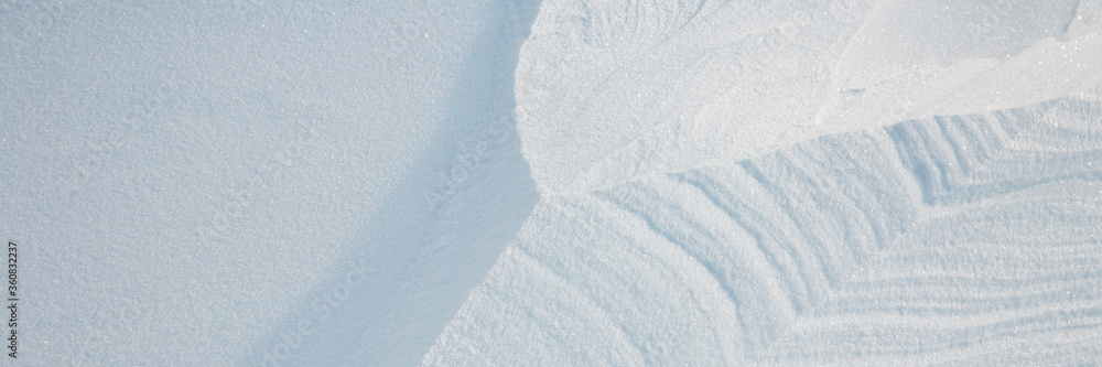 Obraz premium Beautiful winter background with snowy ground. Natural snow texture. Wind sculpted patterns on snow surface. Wide panoramic texture for background and design.
